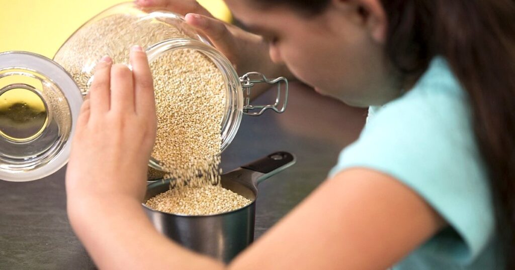 穀物を計量カップに移す子どもの手元